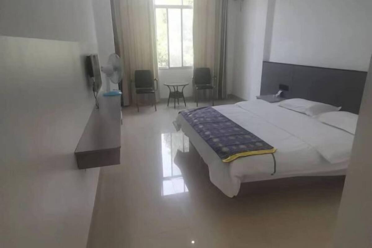 A hotel room with a bed, a bedside table, a chair, a small table, and a window with curtains.