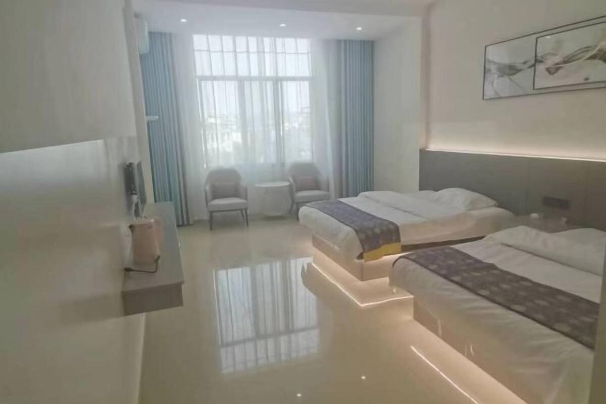 A hotel room with two beds, a small table, a chair, and a window with curtains.