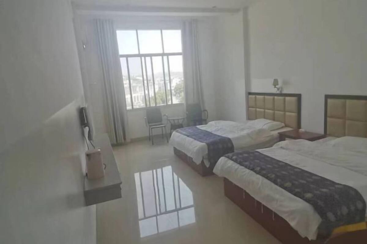 A hotel room with two beds, a chair, a small table, and a window with curtains.