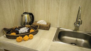 A kitchen with a stainless steel sink, a kettle, and a wicker basket containing coffee cups and a tissue box. - Lumbung Sari Ubud 2

 (Bali)