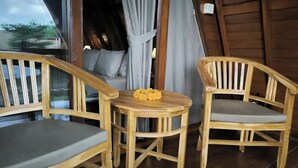 A wooden deck with two wooden chairs and a small round table, a bed with grey curtains, and a wooden door. - Lumbung Sari Ubud 2

 (Bali)