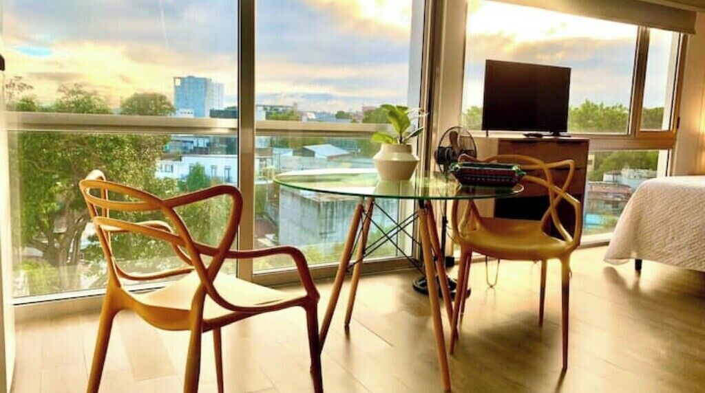 Un balcon avec une table en verre, deux chaises, un téléviseur et une plante en pot.
