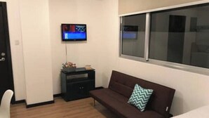 Une petite pièce moderne avec un canapé marron, un téléviseur fixé au mur et une fenêtre.