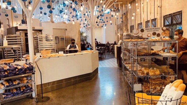 Une boulangerie avec un comptoir où sont exposées des pâtisseries et du pain, un employé et un panneau indiquant un pain de spécialité.
