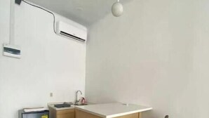 Una cocina compacta con una pequeña isla, dos taburetes de bar, un cubo de basura y un refrigerador pequeño.