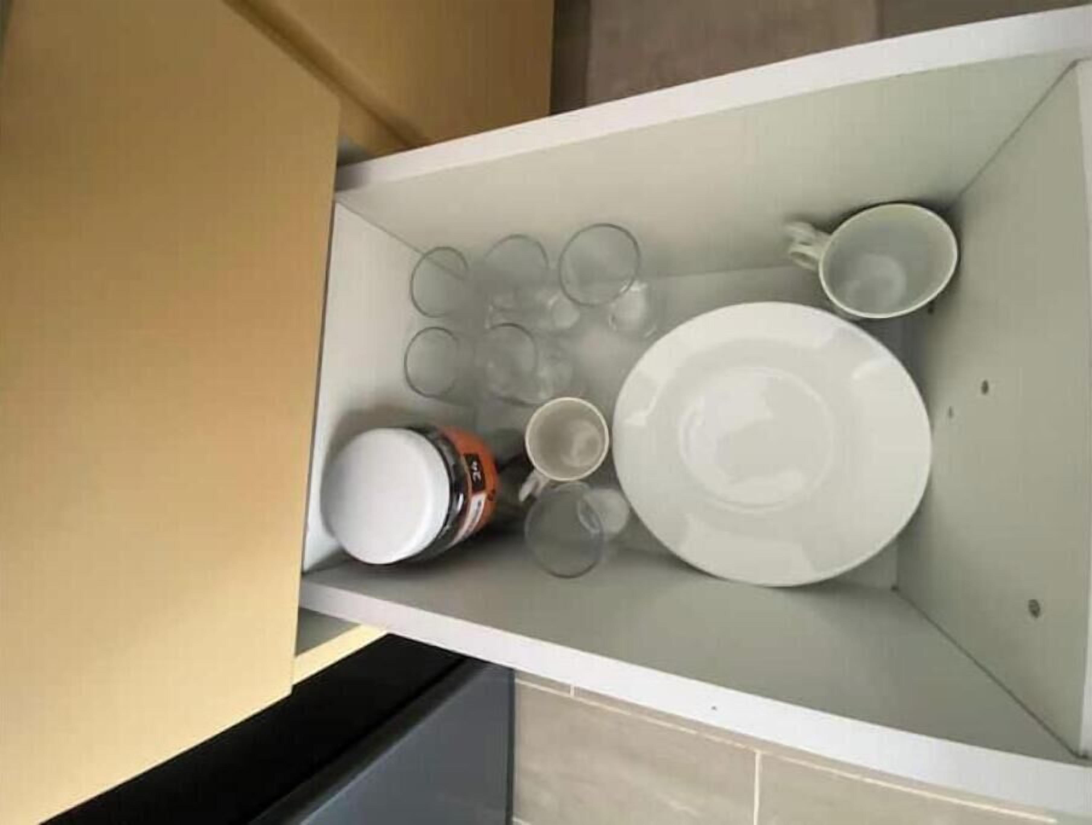 Cuina amb taulell blanc, cafetera, plat i diversos vasos.