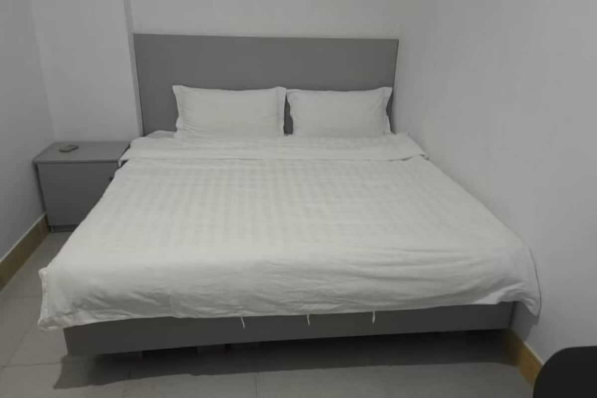 A single-bed room with a grey headboard, white bedding, and a small bedside table.