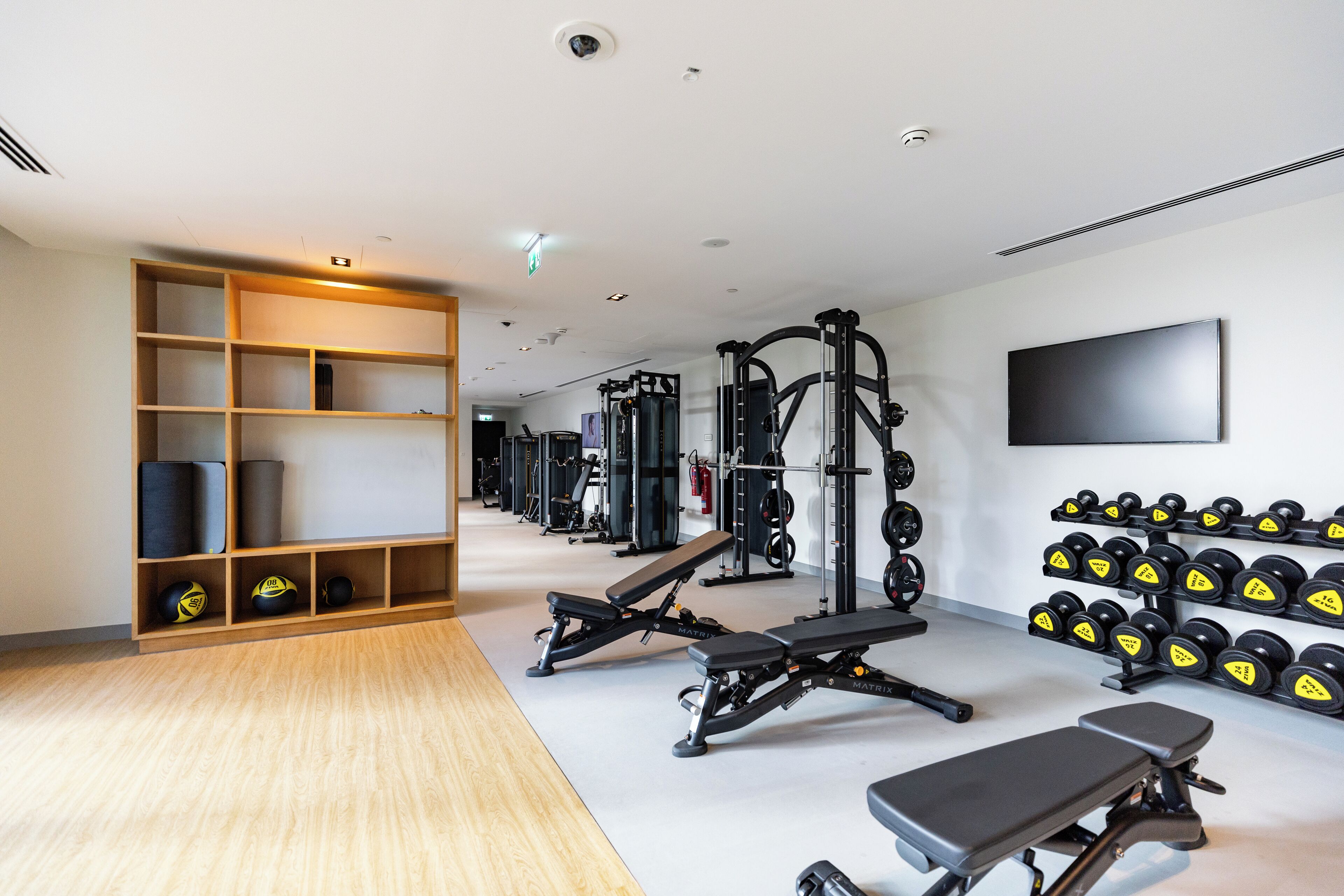 Un gimnasio con equipo de levantamiento de pesas, bancos y mancuernas.