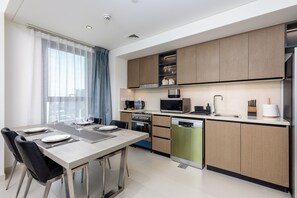 A modern kitchen with a dining area, stainless steel appliances, and wooden cabinets. - Waves - Burj Crown Tower (Dubai)