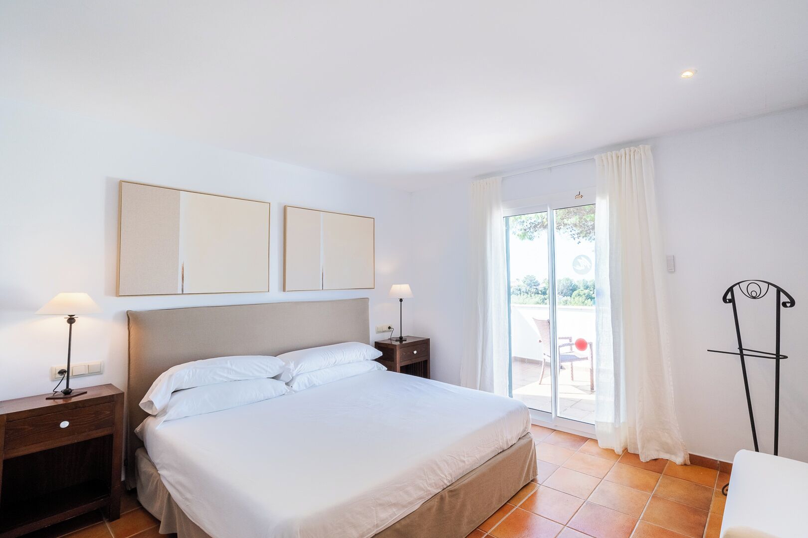 Un dormitorio con una cama, dos mesitas de noche, una butaca y vistas al exterior.