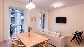 Una sala moderna con una mesa de comedor de madera, un sofá color beige y un televisor de pantalla plana montado en la pared.
