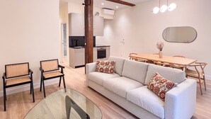 A modern living room with a glass coffee table, a sofa with patterned cushions, and a dining area with a wooden table and chairs.
