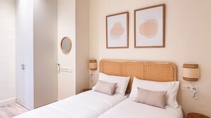 A hotel room with two beds, a wooden headboard, a round mirror, and two framed pictures on the wall.