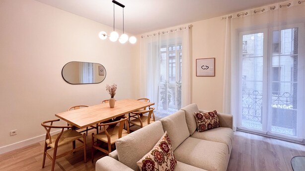 A modern living room with a dining table, sofa, and a large window with a view of buildings.