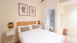 A bedroom with a bed, bedside tables, a nightstand, a mirror, and a shower area.