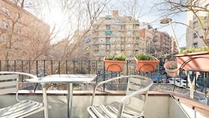 Un balcón con sillas y mesas de metal, plantas en macetas y vistas a edificios de apartamentos.