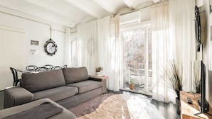 Una sala de estar moderna con un sofá gris, una mesita de noche con una planta y un televisor sobre un mueble de madera.