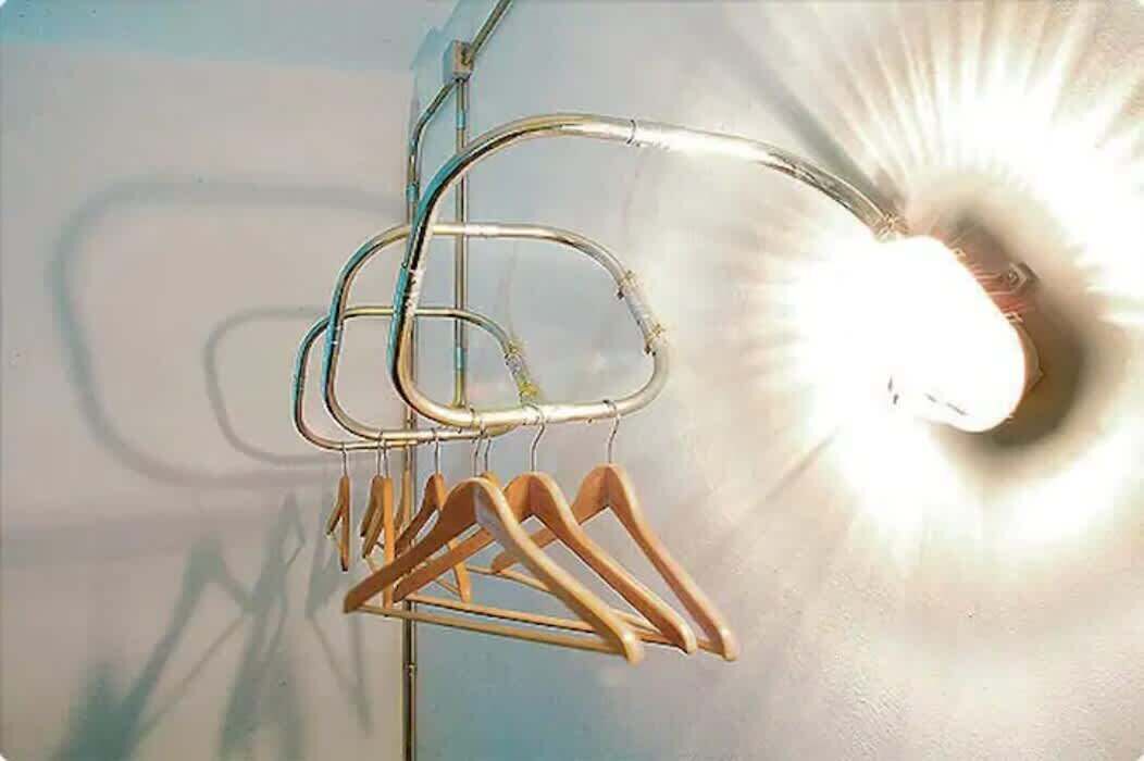 Uma estante de metal com cabides de madeira em frente a uma parede com iluminação intensa.