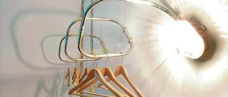 Uma estante de metal com cabides de madeira em frente a uma parede com iluminação intensa.