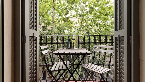 Ein offener Balkon mit Tisch und zwei Stühlen, umgeben von einem Metallgeländer.