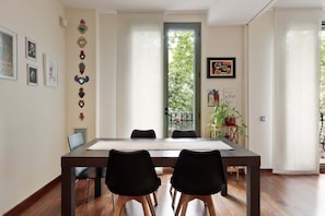 A dining area with a long table, two black chairs, and a view of greenery through a window.