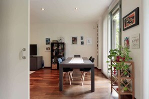 A dining area with a long table, chairs, a bookshelf, and a plant.