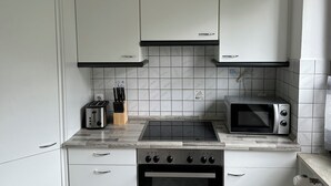 Una cocina compacta con alacenas blancas, estufa a gas, microondas y tostadora.