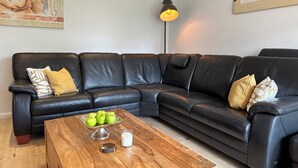 Una sala de estar moderna con un sofá de cuero negro, una mesa de centro de madera con manzanas y un vaso, y una lámpara.