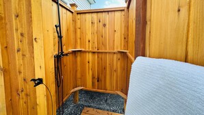 Un área de ducha al aire libre con madera, que incluye un banco, un cabezal de ducha y un perchero para toallas.