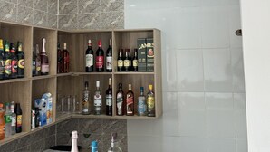 Una zona de bar con estantes llenos de diversas botellas de alcohol, una barra con algunas botellas y una pared de azulejos.