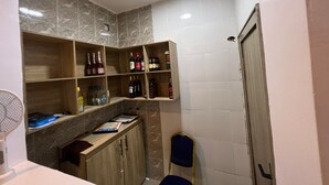 Un baño con pared de azulejos de mármol, estantes de madera con botellas, una silla azul y una puerta blanca.