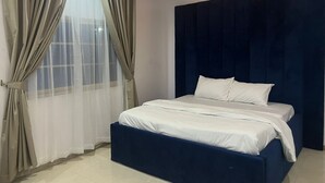 Un dormitorio con cama, cortinas y cabecera oscura.
