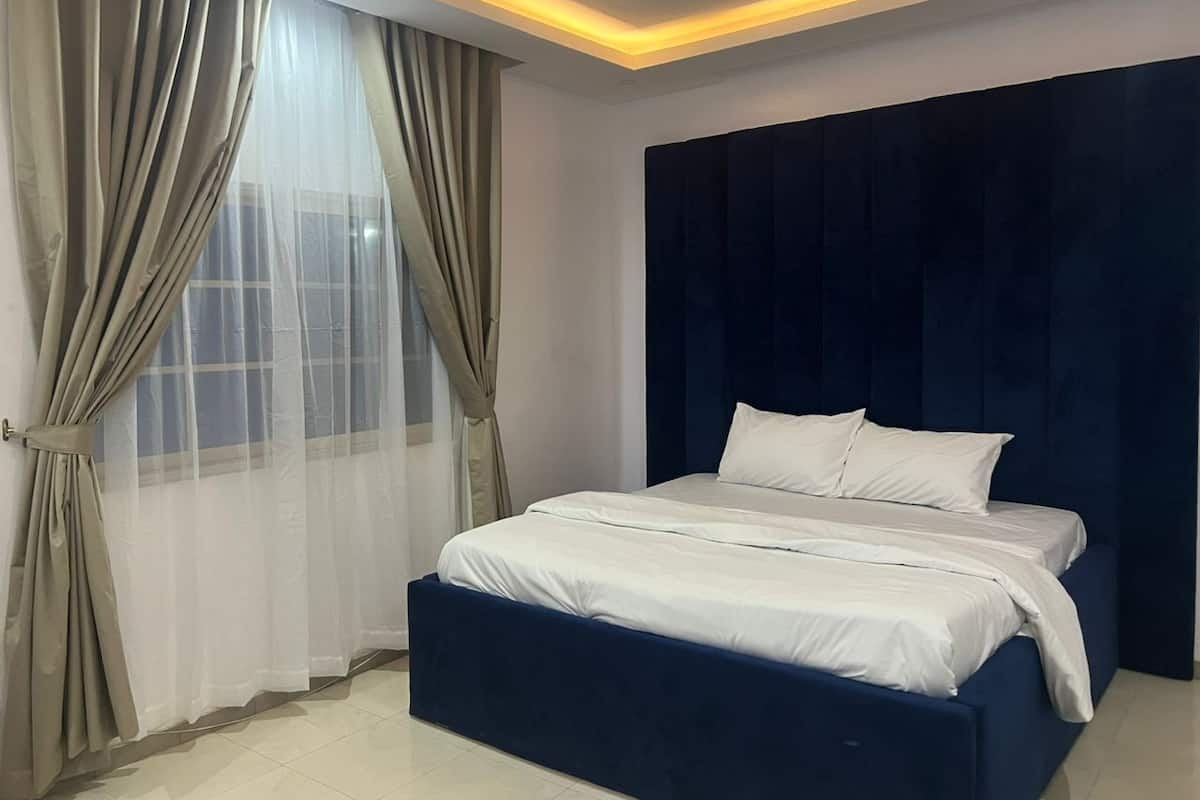 Un dormitorio con cama, cortinas y cabecera oscura.