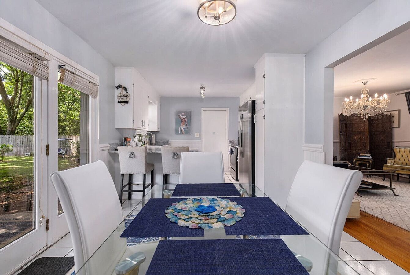 A dining area with a glass table, white chairs, and a blue table runner.
