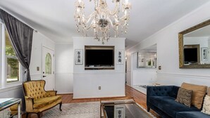 A living room with a chandelier, a television, a sofa, a chair, and a mirror. - Chic Southern Retreat (Charleston)