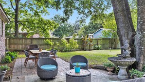 A backyard patio with wicker furniture, a stone fountain, and a wooden fence. - Chic Southern Retreat (Charleston)