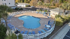 A swimming pool with lounge chairs and a fenced area, surrounded by trees and a building.