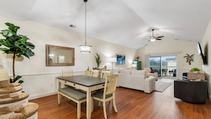 A spacious living area with a dining table, sofas, and a balcony with a view.