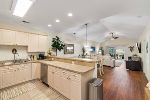 A modern kitchen with a central island, a dining area with a sofa, and a living room with a ceiling fan.