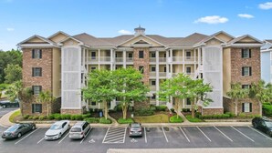 A multi-story hotel with a central courtyard, parking lot, and a mix of brick and stucco exteriors.