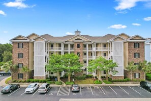 A multi-story hotel with a central courtyard, parking lot, and a mix of brick and stucco exteriors.