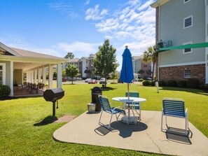 A patio area with a grill, chairs, and an umbrella.