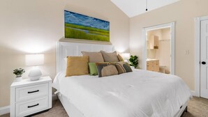 A bedroom with a large bed, bedside tables, a nightstand, a painting, and a door leading to a bathroom.