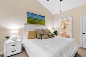 A bedroom with a large bed, bedside tables, a nightstand, a painting, and a door leading to a bathroom.