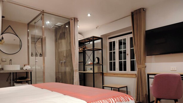 A modern bedroom with a bed, a desk, a chair, a TV, a wardrobe, and a bathroom. - Casa Cruz Verde by Peru Garden Hotels (Cusco)