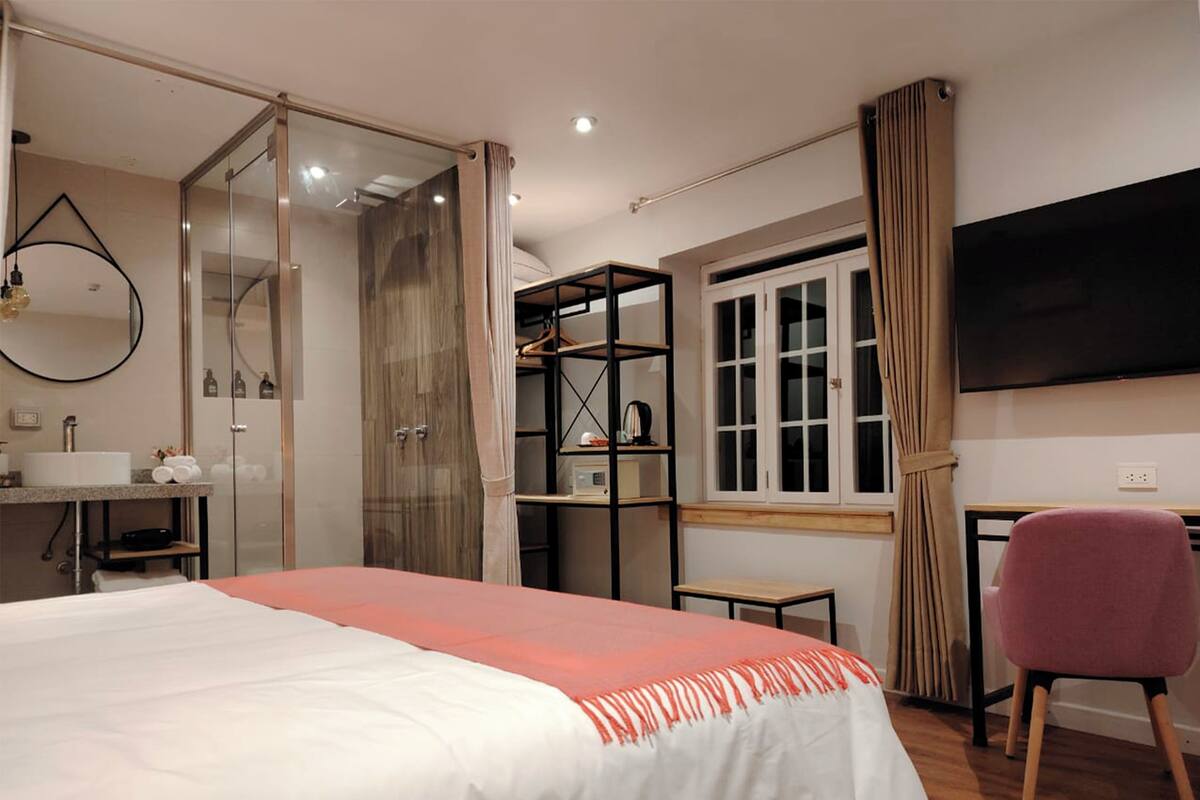Ein modernes Schlafzimmer mit Bett, Schreibtisch, Stuhl, Fernseher, Kleiderschrank und eigenem Badezimmer.