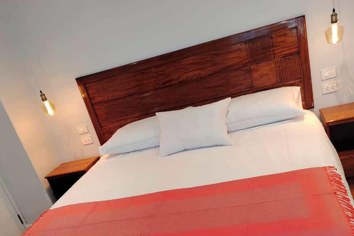 Ein großes Bett mit Holz Kopfteil, weißer und roter Bettwäsche und zwei Nachttischlampen.