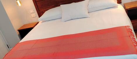 A large bed with a wooden headboard, white and red bedding, and two bedside lamps.