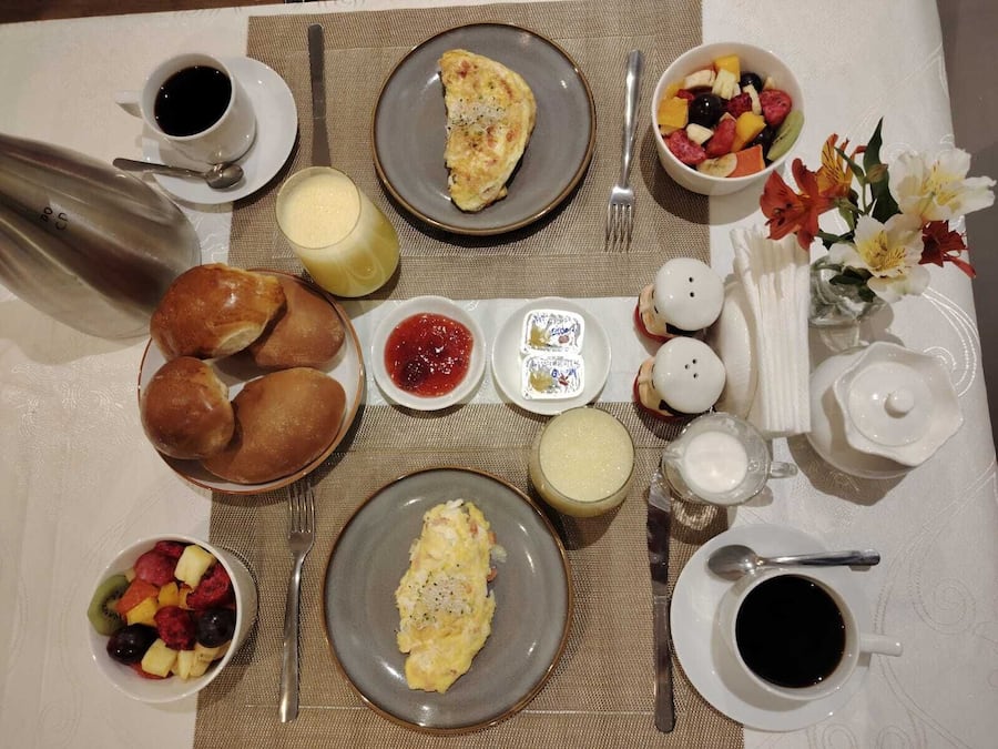 Una mesa de desayuno con diversos platos, entre ellos huevos, pasteles y fruta.