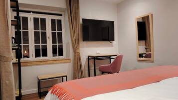 A hotel room with a bed, a desk, a chair, a TV, a window with curtains, and a mirror.